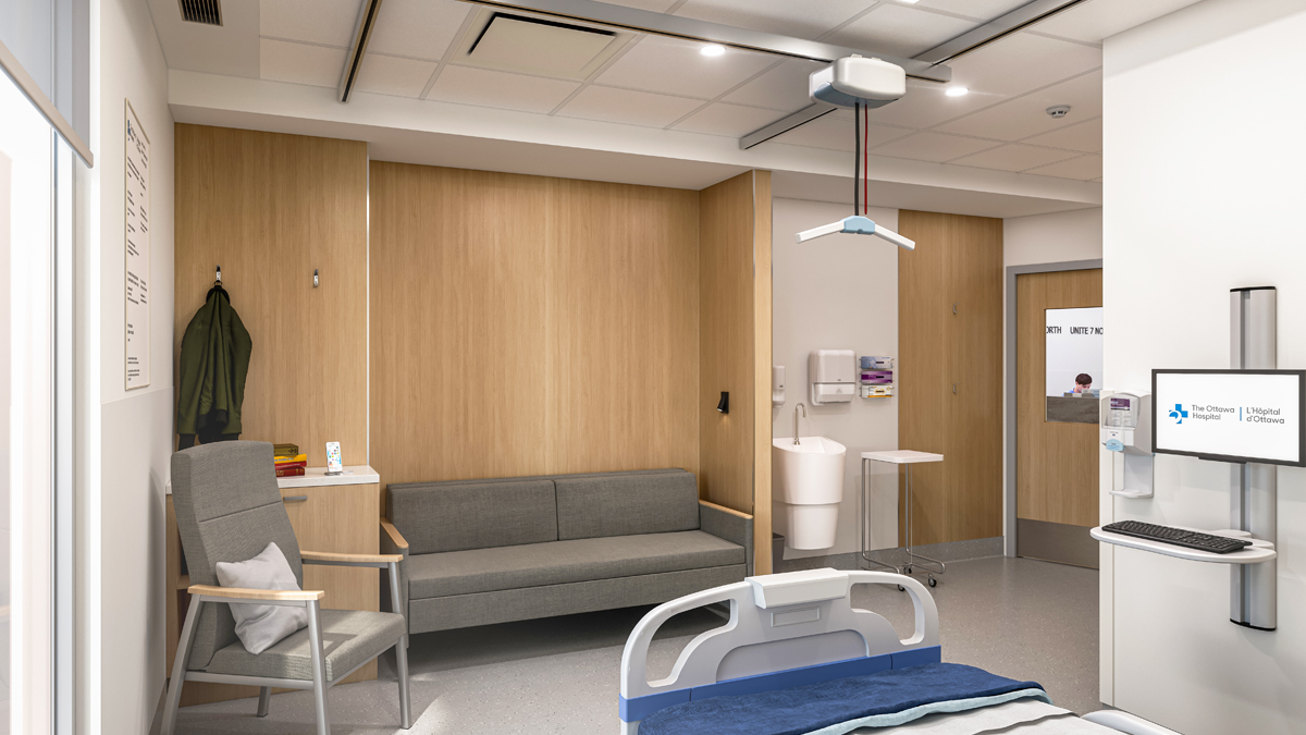 Concept artistique de l’intérieur d’une chambre d’hôpital du nouveau campus de L’Hôpital d’Ottawa du point de vue d’un coin de la chambre, à côté du lit du patient. De gauche à droite, sur le mur en face, on voit une chaise et un canapé, un évier, un moniteur d’ordinateur et un clavier à côté d’un distributeur de désinfectant pour les mains. La porte de la chambre comporte une fenêtre montrant un membre du personnel de l’hôpital dans le couloir. 
